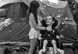 A young girl plays with the hair of a boy in a wheelchair