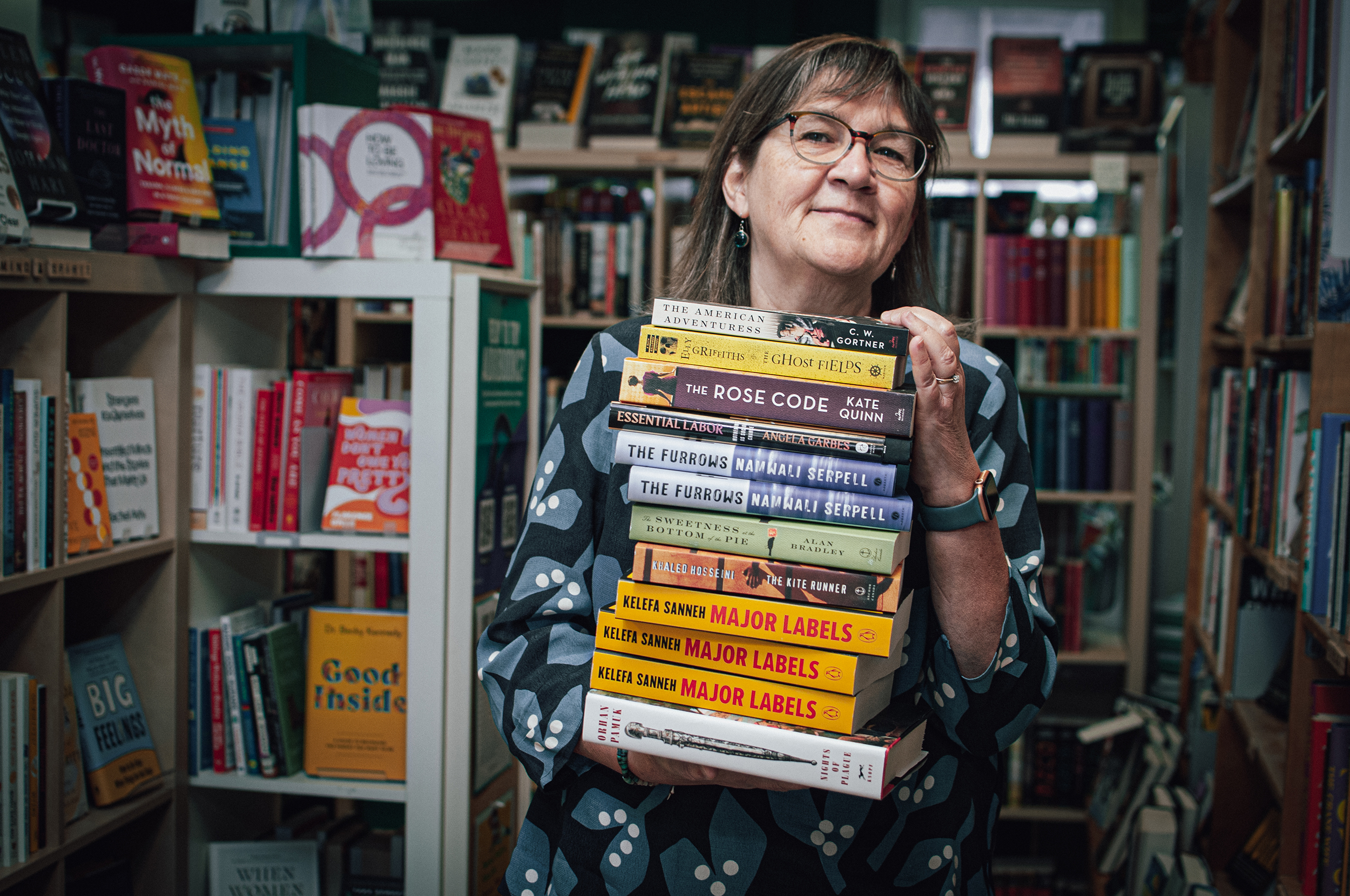 Ann Shea, Owner of Mill Street Books, holds a stack of books.